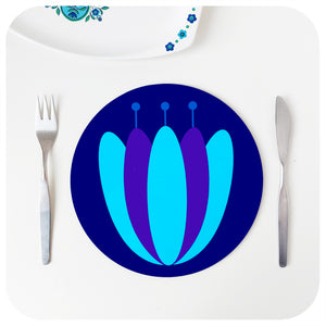 A round retro floral placemat  featuring our tulip design in blues & purples, on a white table with cutlery and vintage serving dish | The Inkabilly Emporium