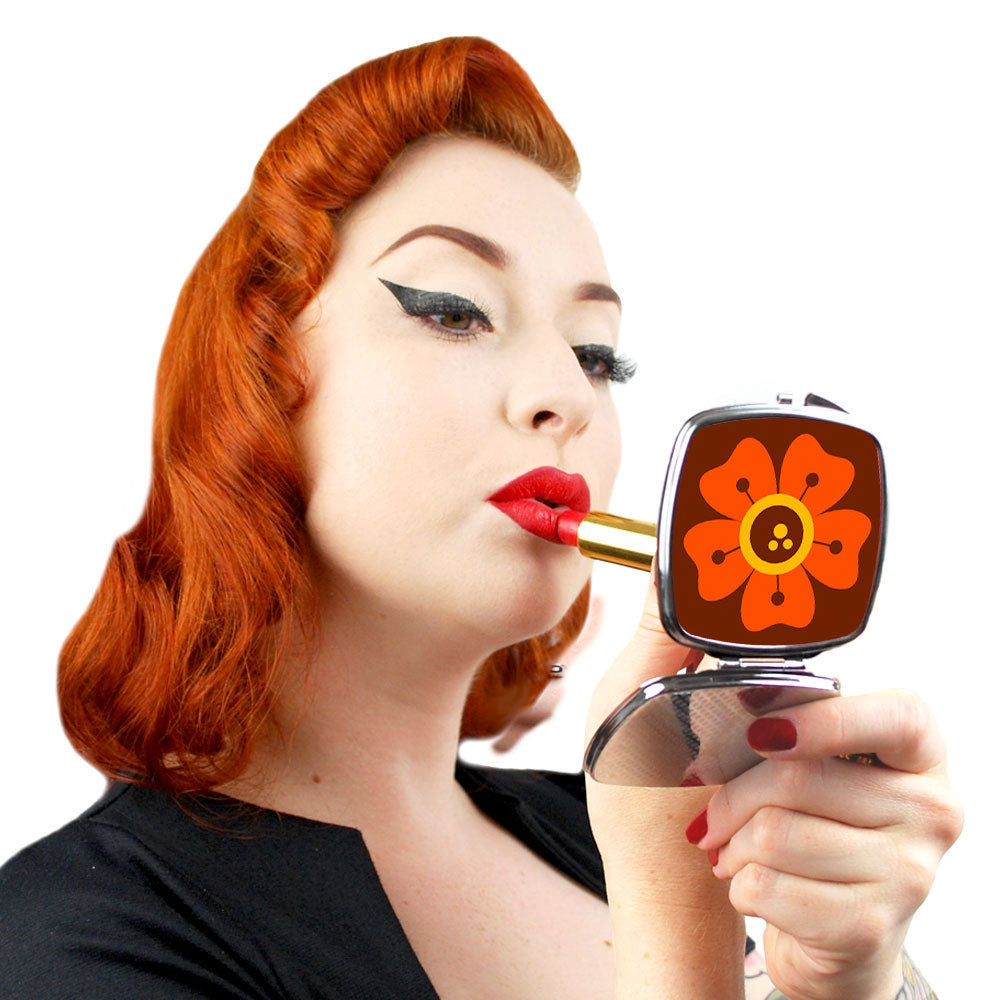 A retro pin-up model puts on her lipstick while looking into a compact mirror with a retro flower design.