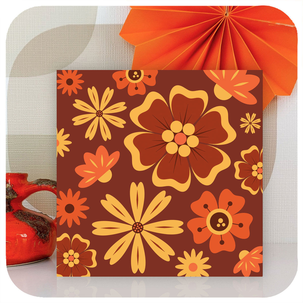 A greetings card with 70s style brown, orange and yellow flowers stands with a small vintage vase and a paper decoration | The Inkabilly Emporium