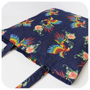 A denim tote bag with printed birds of paradise pattern, lies down on a white background | The Inkabilly Emporium