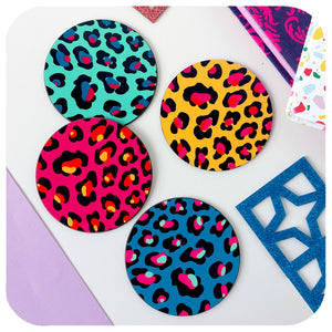 Birdseye view of Four colourful Leopard Print Coasters lie scattered on a white table with books and glittery acrylic shapes | The Inkabilly Emporium